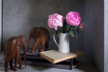 Pink peons in a white porcelain jug on a notebook and a book. Copy space