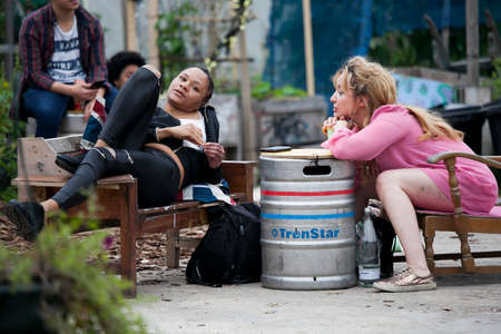 London, UK - 17 July 2019, Nomadic Community Garden. Communal Garden Party. Two girls are sitting in a street cafe. Aluminum barrel used instead of a tableのeditorial素材
