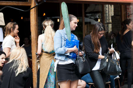 London, UK - 17 July 2019, Columbia Road Flower Market. A girl in a black mini skirt and denim jacket carries a long cactus in a pot through the crowdのeditorial素材