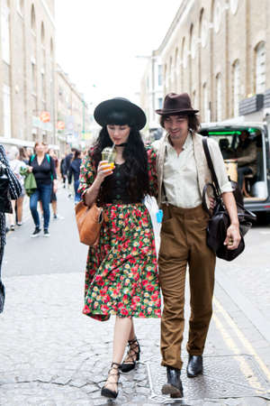 London, UK - 17 July 2019, Fashionably dressed man and woman walk along street. The man has white...