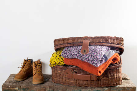Suitcase with warm clothes and boots on wooden surface of bench isolated on white