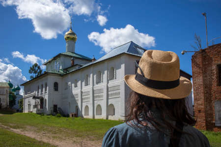 Borisoglebsky, Yaroslavl region, Russia, - 26 July 2020, Orthodox Boris and Gleb monastery. Vintage square at entrance. Back view of brunette girl with long hair in straw hat, green shirt.のeditorial素材