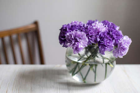 Bridal bouquet of lilac carnations in a round glass vase as table decorationの写真素材