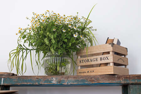 Kitchen decoration. A vase with wild-growing daisies on a shabby bench and a box for storing...