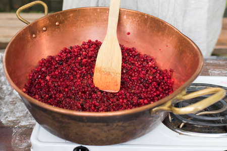 Cooking Finnish lingonberry jam with spices in a copper basin on a gas stoveの写真素材
