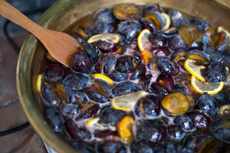 Cooking plum jam with lemon and spices in a copper basin on a gas stove.