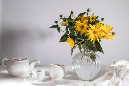 A bouquet of yellow jerusalem artichoke in a transparent vase on against white background on the tableの写真素材