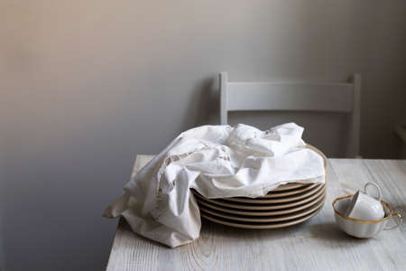 a stack of plates with an embroidered crumpled napkin, two eggs and two empty tea cups on a gray wooden kitchen table. Copy spaceの写真素材