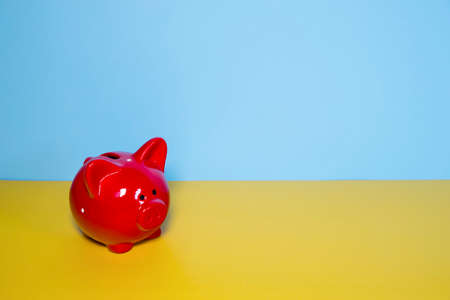 Red pig piggy bank in a white speck on a yellow table against the background of a blue wall. Space for text. Wealth concept. Copy spaceの写真素材