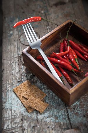 Hot chili peppers on a fork in a wooden mango tree box on a wooden bench. Copy space.Top viewの写真素材