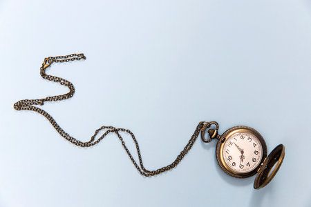 A pocket watch on a chain is on a blue background as a decoration or a design card. Copy space