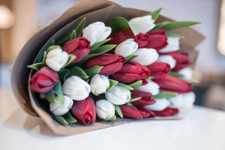 A bouquet of white and dark red tulips wrapped in gray craft paper lies on the table. Spring timeの写真素材