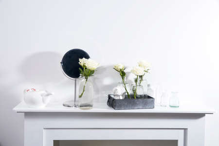 Bouquet of white roses in a glass figured vase on a white fireplace console. A faience figurine of angel as an interior decoration. Copy space. Rose White Pink O'hara.の写真素材