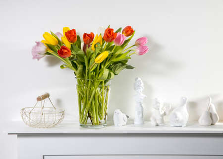 A bouquet of multi-colored tulips in a transparent vase and cup of tea on the white table. Copy spaceの写真素材