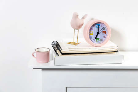 an alarm clock showing seven o'clock, cup, a pink bird figurine, a books on the table. Scandinavian...
