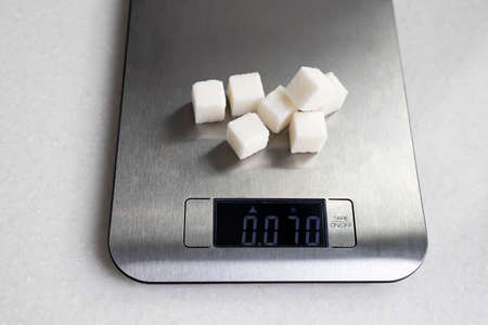 Seven lumps of refined sugar are weighed on a kitchen scale. Diet.の写真素材