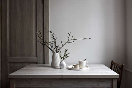 Minimalistic Scandinavian style. Half-open branches of an apple tree in a white fluted vase. A small vase with a branch of dried eucalyptus and two cups of coffee on a tray on the table.の写真素材