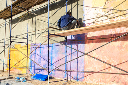 Moscow, Russia - 08 May, 2021, A worker paints the wall of a building while sitting on the scaffolding.のeditorial素材
