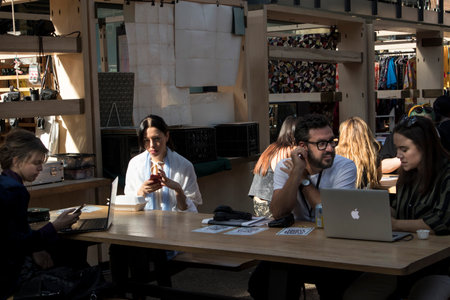 LONDON, UK - December 22, 2020, Spitalfields market. Young people are sitting at a table in a food court in the market. The girl eats from a cardboard box. Man with woman with laptops discussing workのeditorial素材