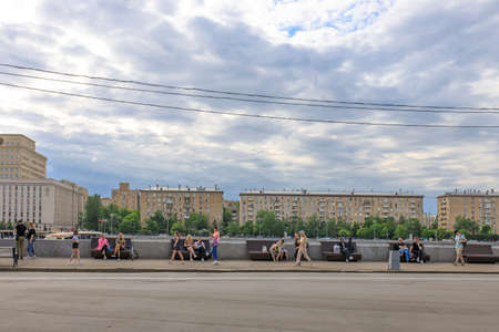 Moscow, Russia - May 15, 2021: View of Pushkin embankment. People sits on log by the river. ship sails under the bridge. Mother and child stand by the steps. Gorky Central Park of Culture and Leisureのeditorial素材