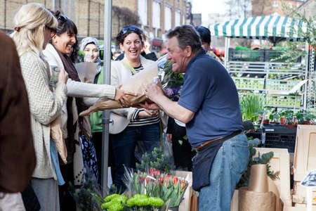 LONDON, ENGLAND - October 12, 2018 People buying flowers at Columbia Road Flower Market. The seller...
