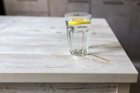 Transparent glass tables with a slice of lemon is on a wooden table in a beige kitchen interior. Empty spaceの写真素材