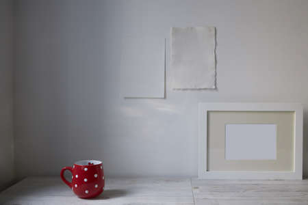 Scandinavian style. Interior Design. A red cup in the dot, a frame for a photo are on the table. Two blank sheets of paper are attached to the wall. Empty space for textの写真素材