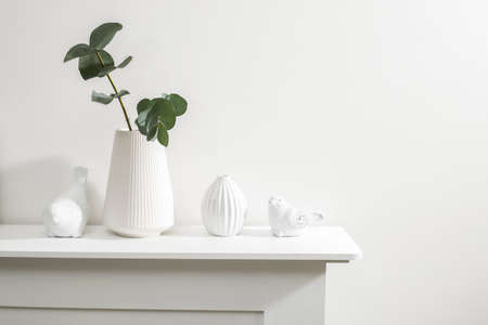 Figurines of a bird are on the surface of the chest of drawers. A vase with a eucalyptus branch....