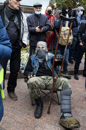 Moscow, Russia - 25 September 2021, Hundreds of Russians protest over last week's parliamentary elections. A man in a mask in camouflage clothes with broken leg sits in chair, listening to speakersのeditorial素材
