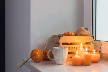 Preparing your home for Halloween. A wooden pumpkin box, a faux pumpkin garland, orange candles, a cup of tea and a candle lantern decorate the window.の写真素材