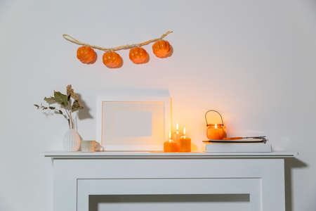 Preparing your home for Halloween. A garland of pumpkins on the wall above fake dresser panel. Frame with the inscription, orange candles and lantern. Corrugated vase with dried eucalyptus branch.の写真素材