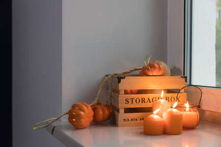 Preparing your home for Halloween. A wooden pumpkin box, a faux pumpkin garland, orange candles, a cup of tea and a candle lantern decorate the window.の写真素材