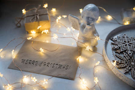 Apartment decoration for Christmas. A plaster figure of an angel is on a beige envelope with congratulations. An asterisk garland shines all over the frame. Copy spaceの写真素材