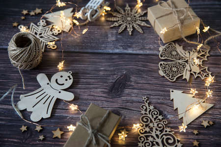 Glowing garland star, two gray boxes with gifts tied with twine, plywood Christmas decorations carved from wood on a wooden table surface. Copy spaceの写真素材