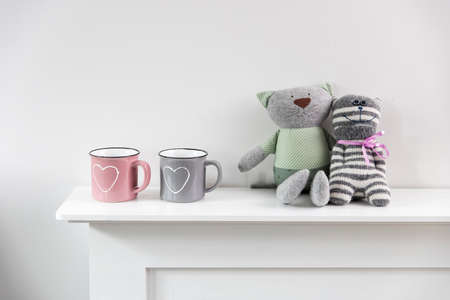 A pink and gray mug with a painted white heart, two funny toy rag cats are positioned on the fireplace. Home decoration for Valentine's Day. Scandinavian styleの写真素材