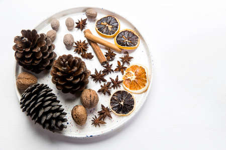 Christmas composition in a bowl. Cones, nutmeg, cinnamon, dried orange slices, anise, walnuts on a tray as home decoration for the New Year on the white wooden tableの写真素材