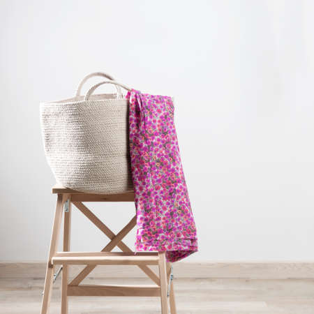 Large gray beach bag with a pink pareo woven from canvas on a beige stool against a white wall. Place for textの写真素材