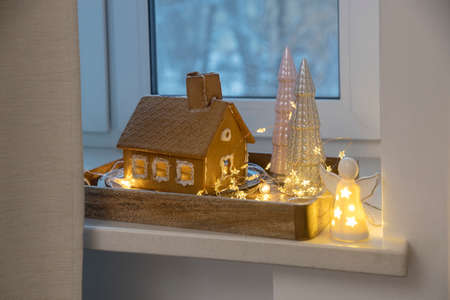 A gingerbread house, gray and pink ceramic Christmas trees, an angel figurine and a garland decorate the window for Christmas.の写真素材
