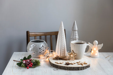 A cup of coffee on a wooden stand, ceramic Christmas trees in pastel colors, gingerbread cookies, gray candlestick. Artificial spruce branch with red berries. Scandinavian style. Copy space.の写真素材