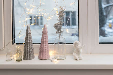 Gray and pink ceramic Christmas trees, a glass bottle with an artificial silver branch and a garland...