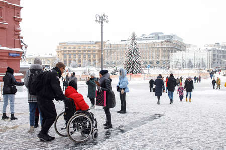 Moscow, Russia - 20 December 2021, A woman carries a man in a red jacket with a disability in a wheelchair across the Red Squareのeditorial素材