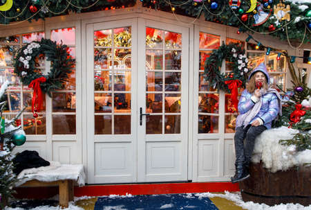 Moscow, Russia - 20 December 2021, Girl posing by a decorated Christmas tree in front of a small gift shop.Fair-GUMのeditorial素材