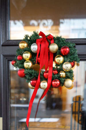 Christmas wreath of fir branches with decorations, flowers of cotton hanging on the transparent door of the houseの写真素材