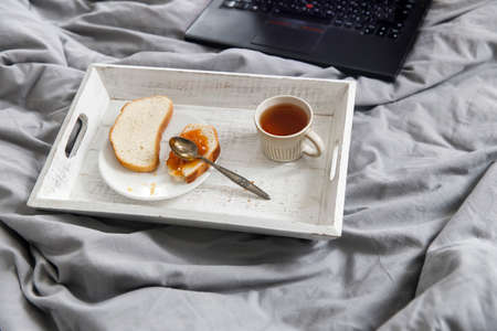 A teapot, a cup of tea, two slices of toasted bread with apricot jam on a tray on the bedside table.の写真素材