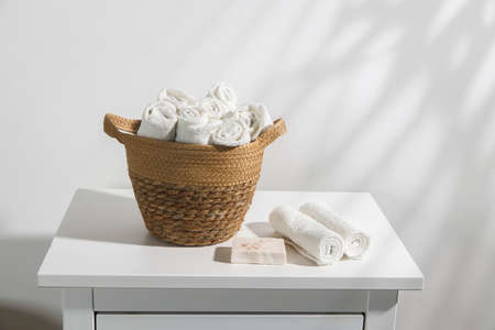 A wicker basket with face towels rolled up on a chest of drawers. The shadow of a palm leaf. Place for textの写真素材