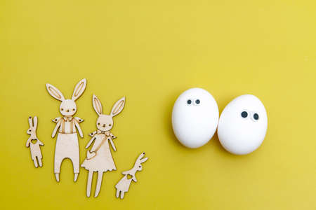 Family of funny hares cut out of plywood are on the yellow background. A cheerful white eggs with...