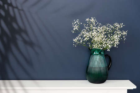 A large glass green jug with a bouquet of gypsophila are on a white table chest of drawers. Place for text. copy spaceの写真素材