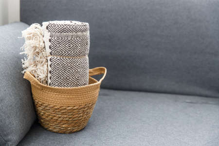Tweed plaid rolled up in a wicker basket on a gray sofaの写真素材