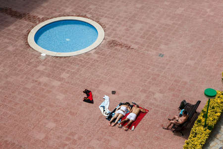 Blanes, Catalonia, Spain. - 25 July 2017, Top view of a small children's round municipal swimming pool in a residential complex. People lie on a towel and sunbathe.のeditorial素材