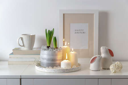Unblown hyacinths with burning candles and artificial ice on a tray, a stack of books, a mug of tea, two ceramic figurines with hares. easter room decoration.の写真素材